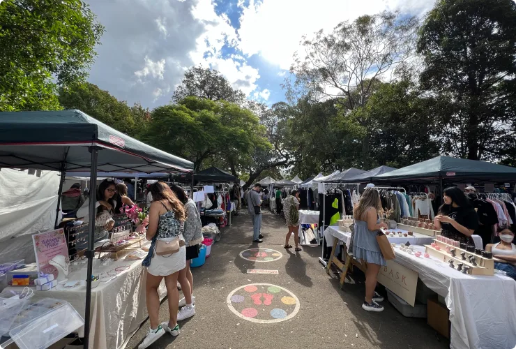 Outdoor market stalls with shoppers on sunny day.